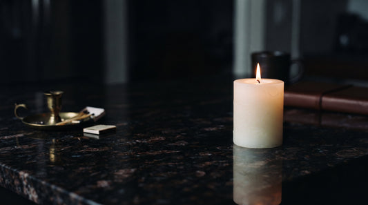 Lit pillar candle on a dark polished surface with warm golden light
